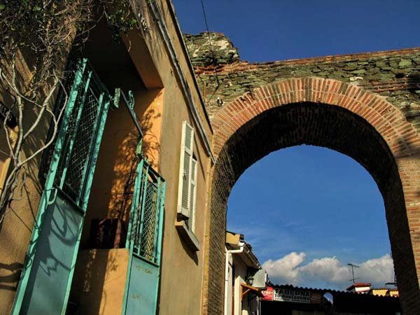 A historic stone and brick archway in Upper Thessaloniki next to a traditional house with a teal gate