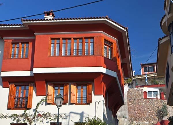 Traditional Macedonian house in Ano Poli with a vibrant red overhanging upper floor and wooden window shutters