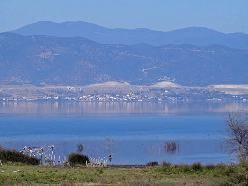 Panoramic view of Lake Volvi with a village on the far shore and blue mountains rising behind it