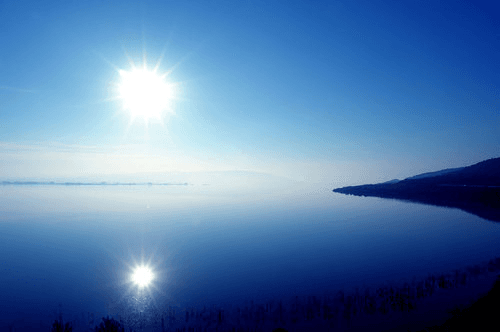 Sun shining over the tranquil, blue waters of Lake Volvi with a clear reflection on the surface