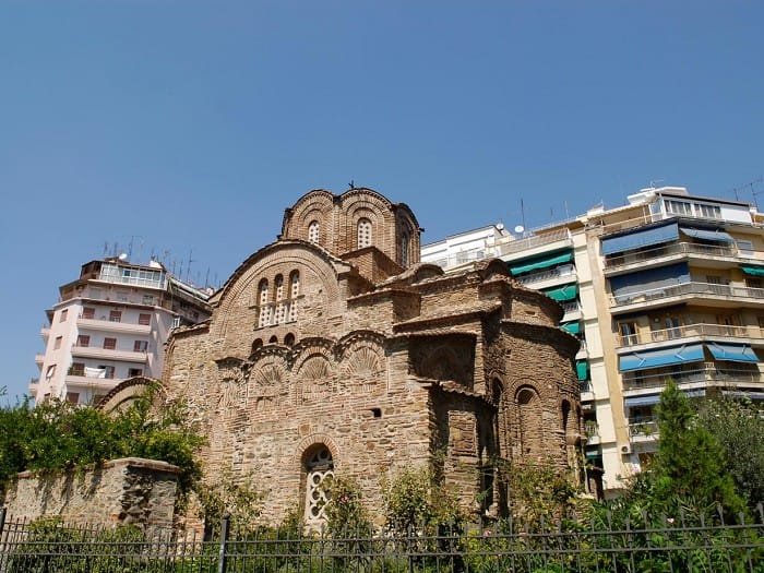 Byzantine stone Church of Agios Panteleimon with multiple domes, situated next to modern apartment buildings