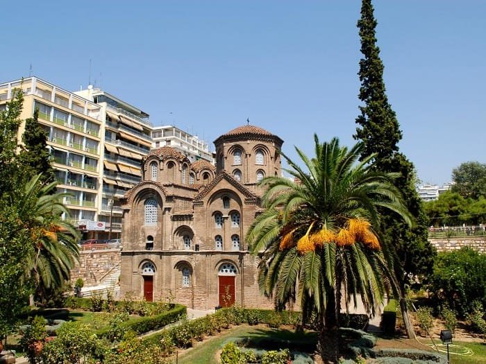 The red brick Byzantine Church of Panagia Chalkeon with its domes, surrounded by palm trees and modern buildings