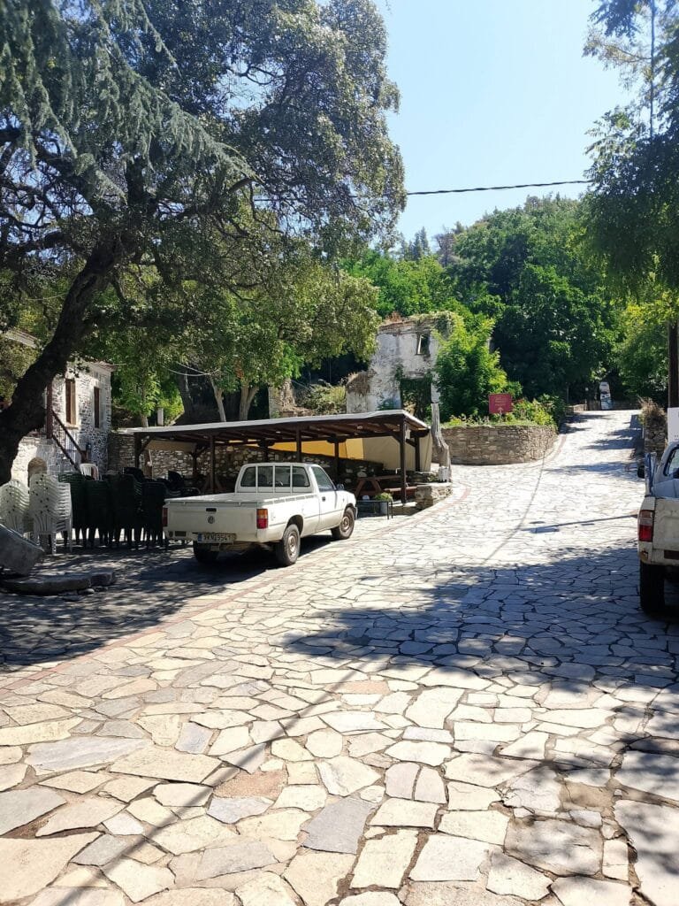 Stone-paved street in Parthenon village with traditional stone buildings, ruins, and lush green trees