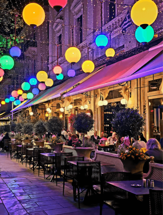 Outdoor cafe along a Thessaloniki street at night, illuminated by colorful glowing spherical lights overhead