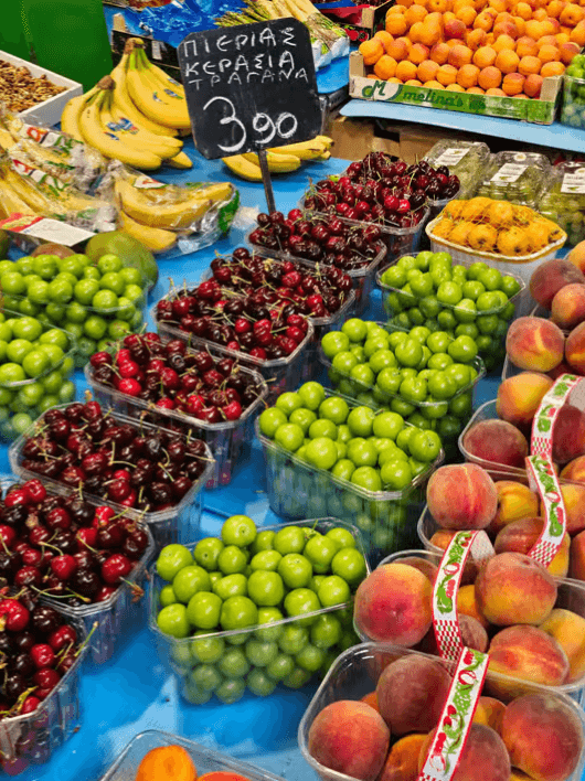 Fresh cherries, green plums, peaches, and bananas on display in plastic containers at a market stall