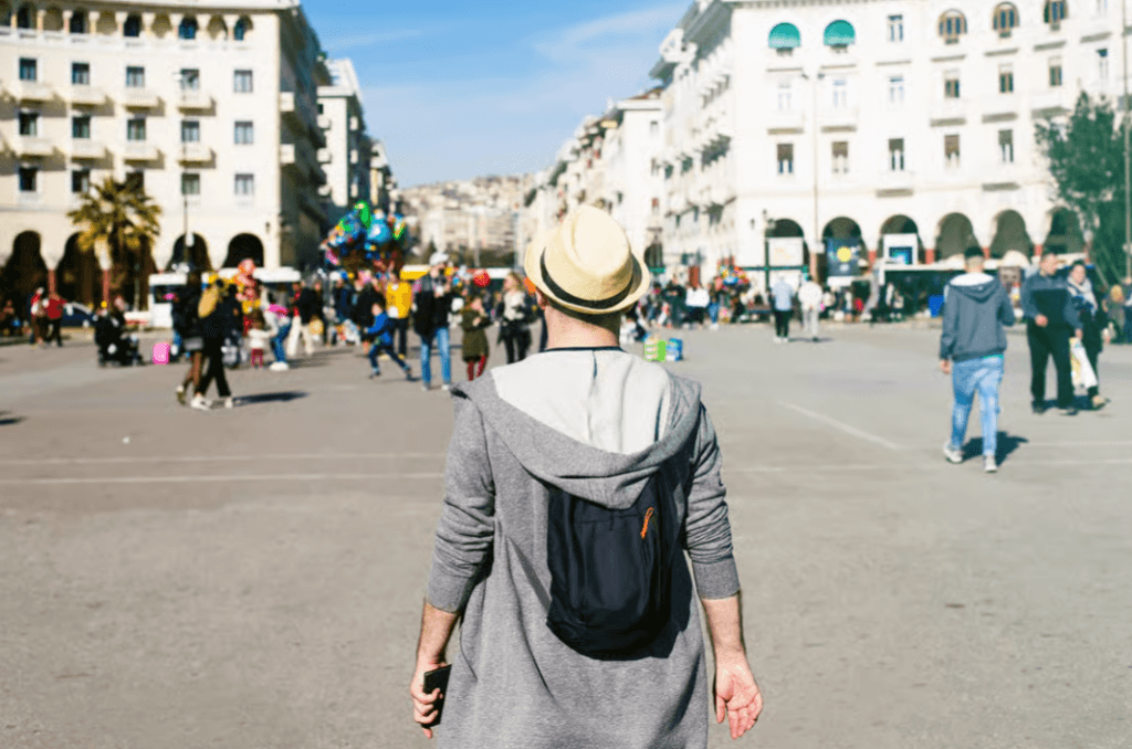 A traveler with a backpack and hat looks out over a busy city square in Thessaloniki
