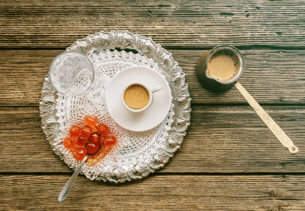 Traditional Greek coffee served on a silver tray with a glass of water, spoon sweets, and a briki