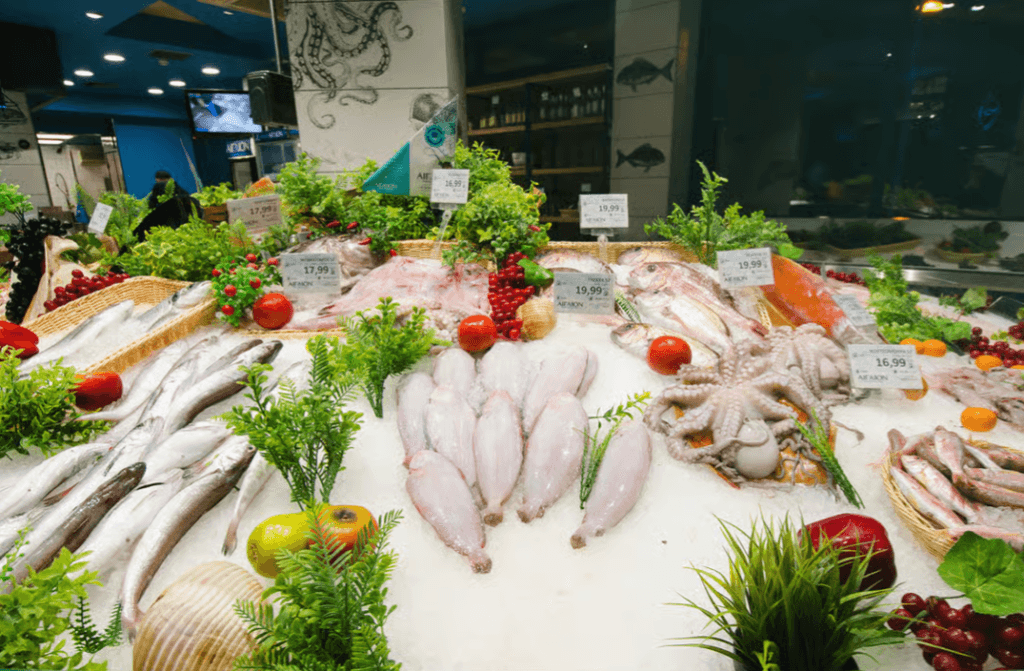 Fresh fish and octopus displayed on ice with price tags and decorative greenery at a Thessaloniki market