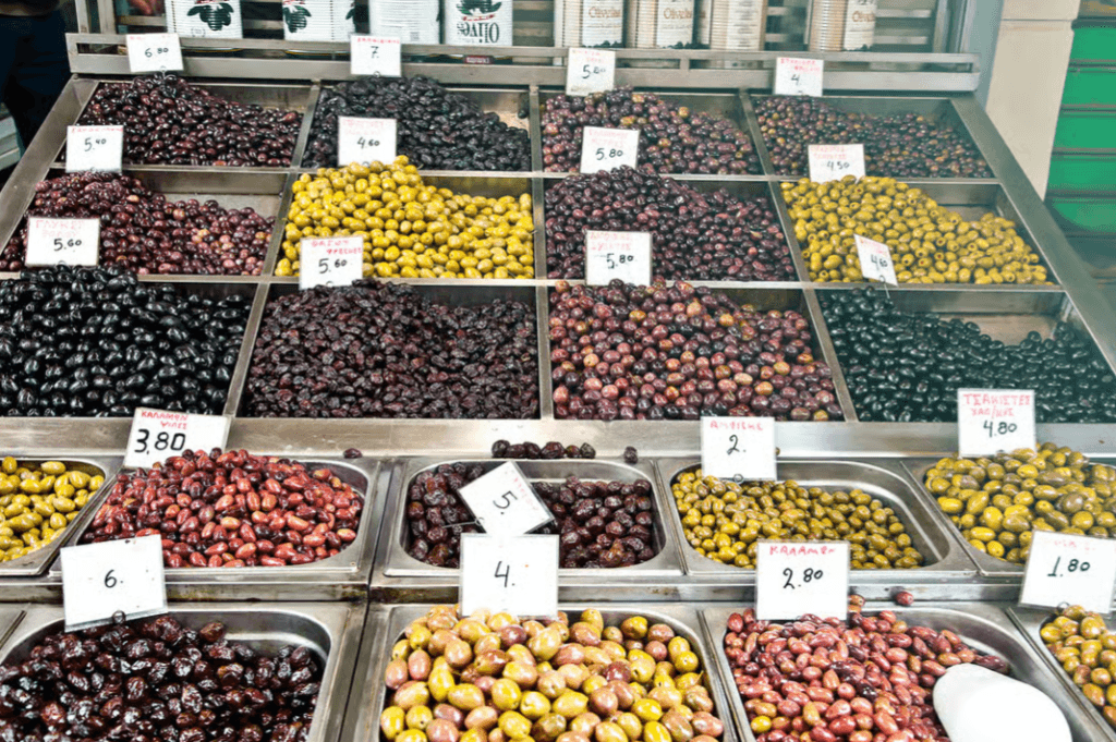 A variety of green, black, and brown olives displayed in metal bins with price tags at a market stall