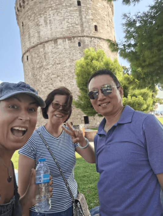 A local guide and two travelers smiling for a selfie in front of the White Tower of Thessaloniki
