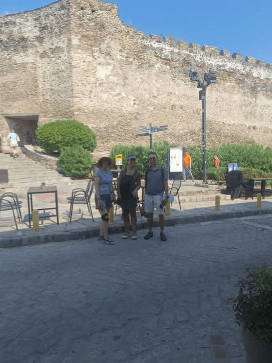 Three people on a walking tour in front of a historic stone fortification in Thessaloniki