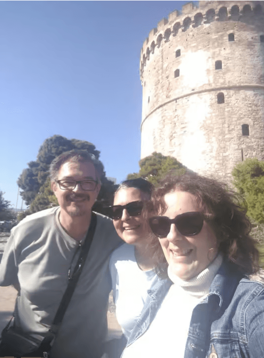 Three people smiling in front of the White Tower of Thessaloniki during a walking tour