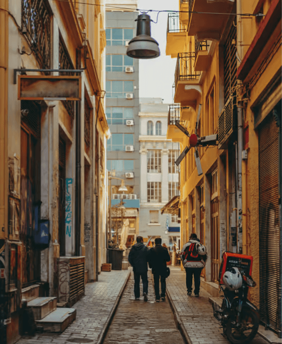 Three people walking down a narrow, sunlit street in Thessaloniki with historic buildings and a hanging lamp