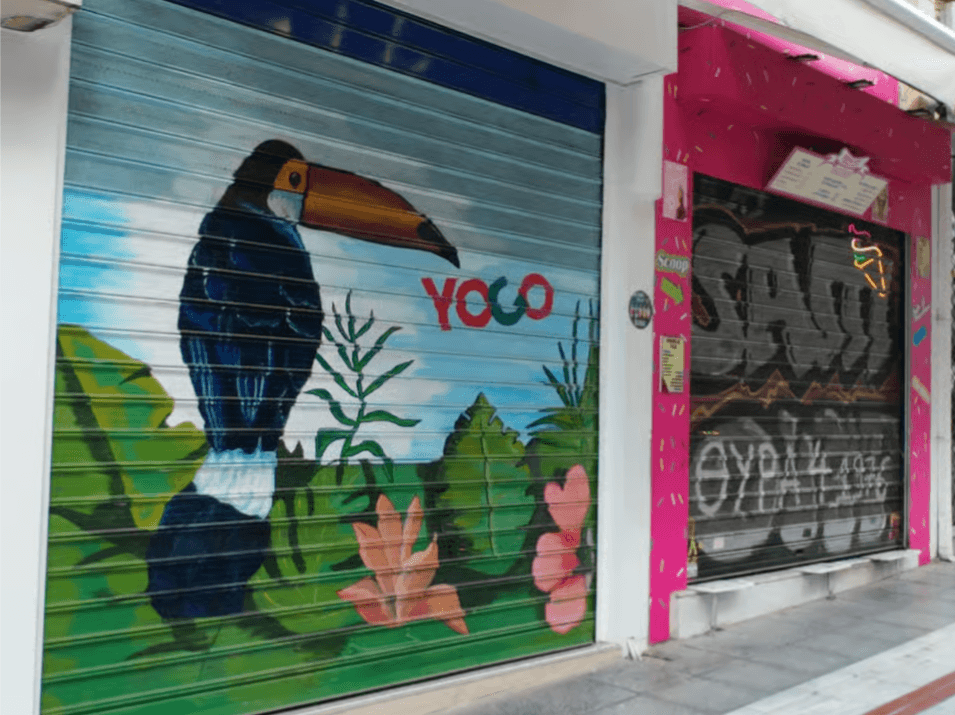 Street art in a Thessaloniki alley featuring a toucan mural and a pink storefront with graffiti