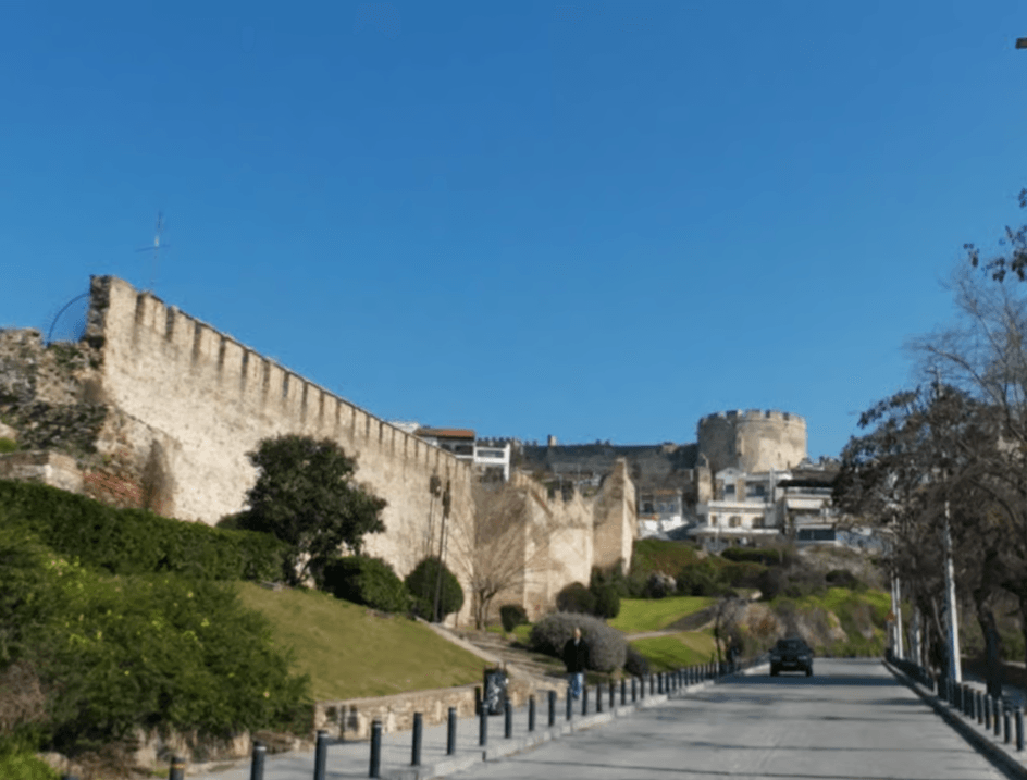 Ancient stone fortification walls and a round tower on a grassy hill in the Ano Poli district of Thessaloniki