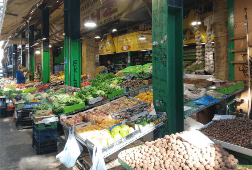 Vibrant market stall in Thessaloniki displaying crates of fresh produce, leafy greens, and walnuts