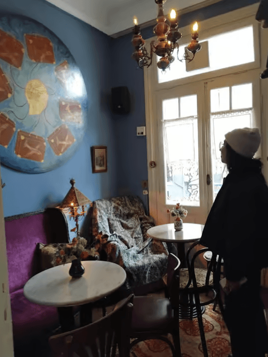 Cozy interior of a Thessaloniki cafe with blue walls, marble tables, eclectic furniture, and large circular art