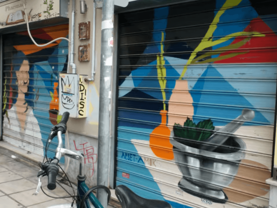 Colorful murals of a woman and a mortar and pestle painted on metal shop shutters in a Thessaloniki alley