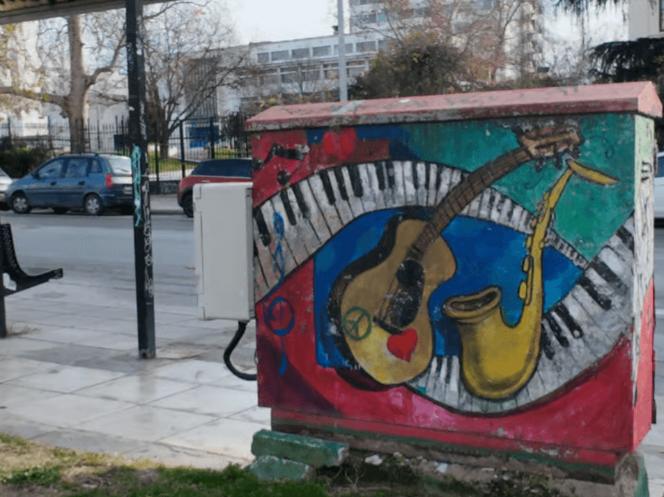Colorful street art on a utility box featuring a guitar, saxophone, piano keys, a heart, and a peace sign