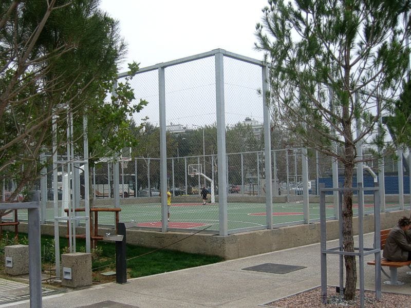 Fenced outdoor basketball court in the Garden of Remembrance, surrounded by trees and a paved walkway