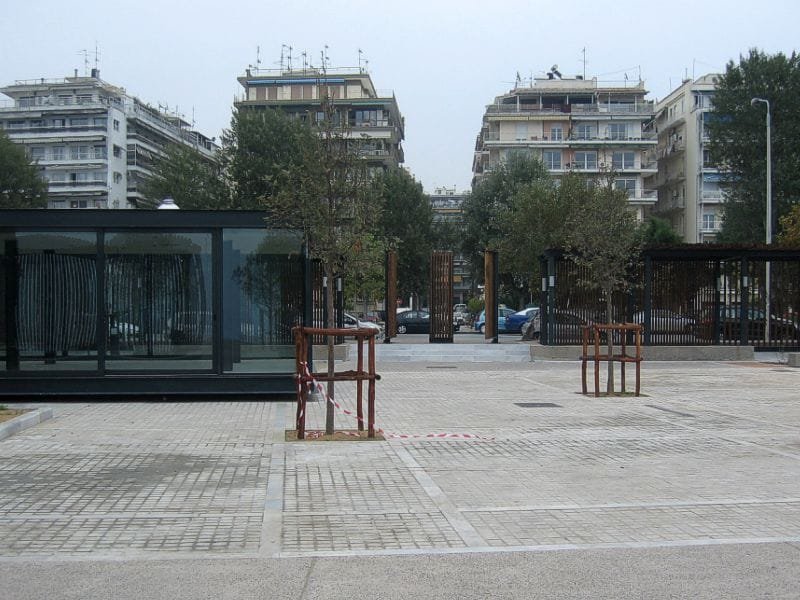 Modern glass refreshment stand on a paved plaza with young trees and a perimeter pergola in the Rose Garden