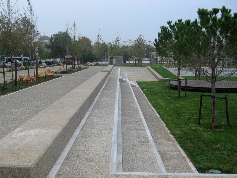 Modern landscaped park with concrete seating tiers, paved walkways, and young trees in a grassy clearing