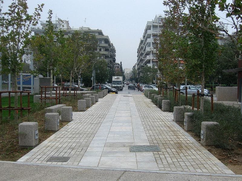 A paved walkway in the Garden of Remembrance lined with rows of trees, leading toward city buildings