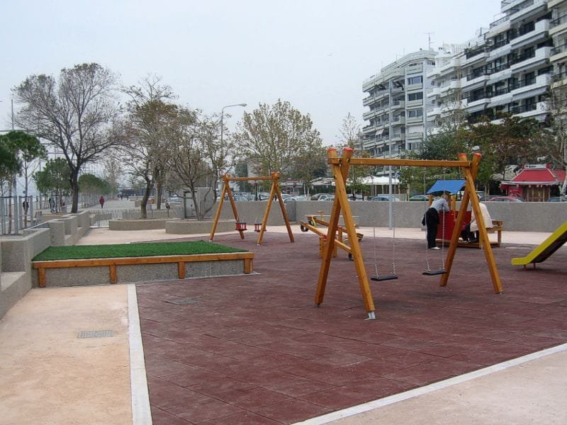 Children's playground with wooden swings and a slide on red safety tiles at the Garden of Music
