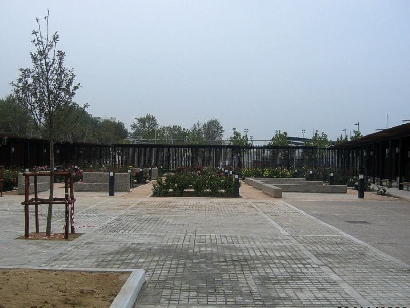 Paved courtyard of the Rose Garden with rose bushes, stone benches, and a dark wooden pergola