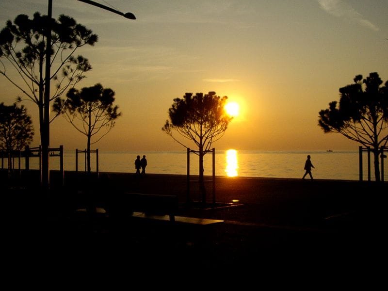 Silhouetted people and trees on the Thessaloniki promenade during a sunset over Thermaikos Bay
