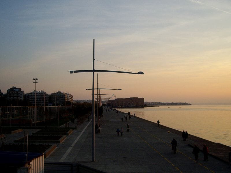 Thessaloniki beachfront promenade at sunset with modern streetlights, people walking, and the sea