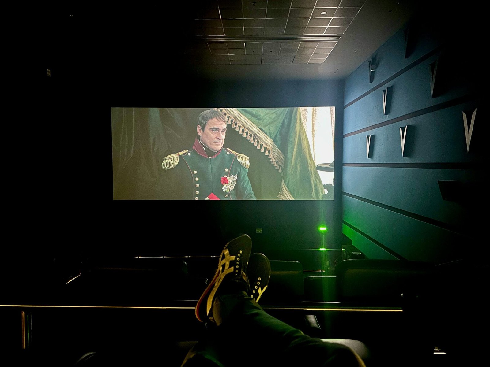 A movie screening in a dark theater with a person's feet propped up in the foreground